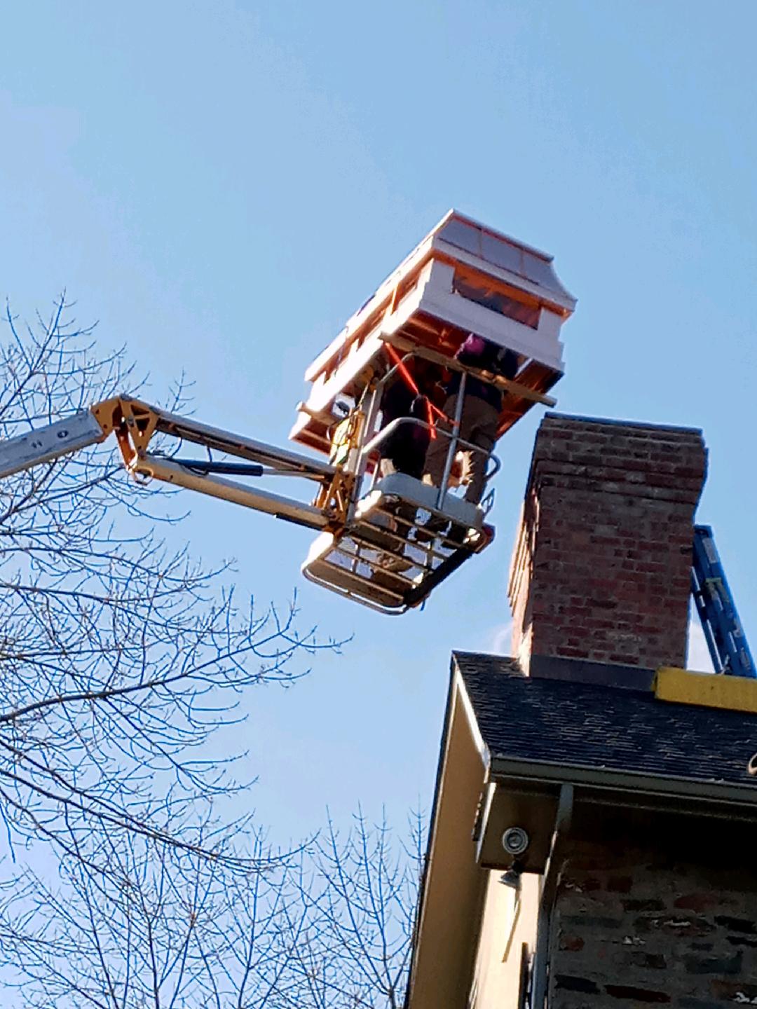 Custom chimney cap being installed on brick masonry chimney via bucket truck — professional chimney topper installation