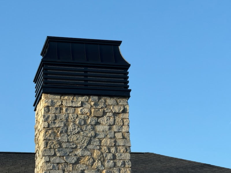 Custom louvered Kynar aluminum chimney cap on stone masonry chimney — wind-resistant design, hand-fabricated by Archaic Metal