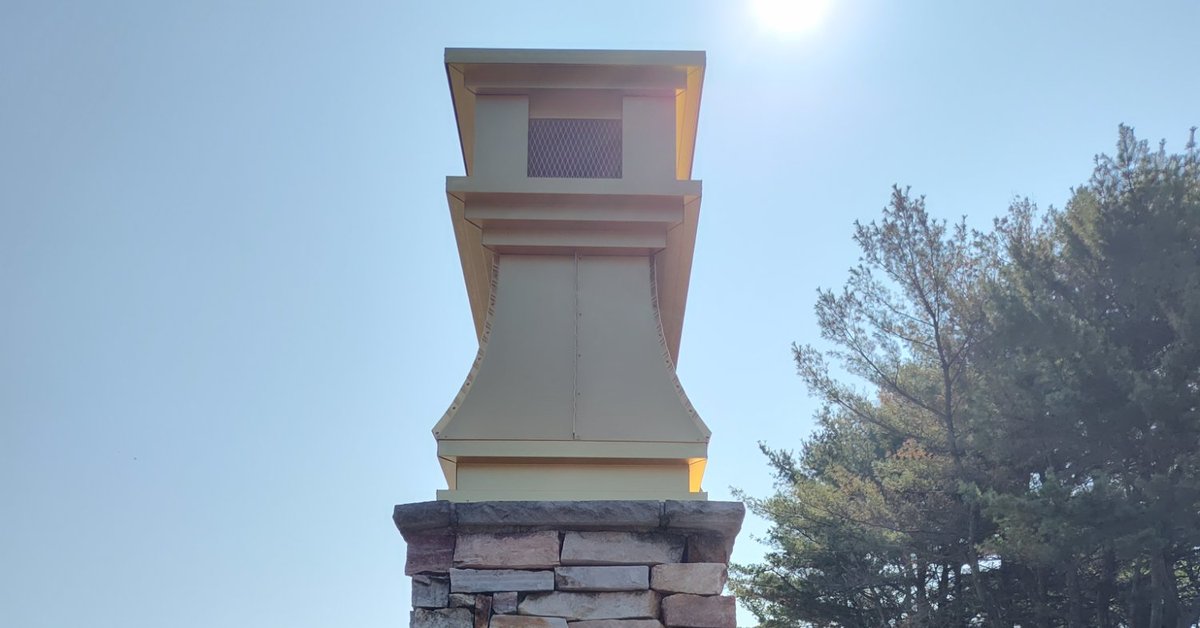 Gold anodized aluminum curved panel chimney cap installed on stone chimney — custom fabricated by Archaic Metal, Berlin NJ