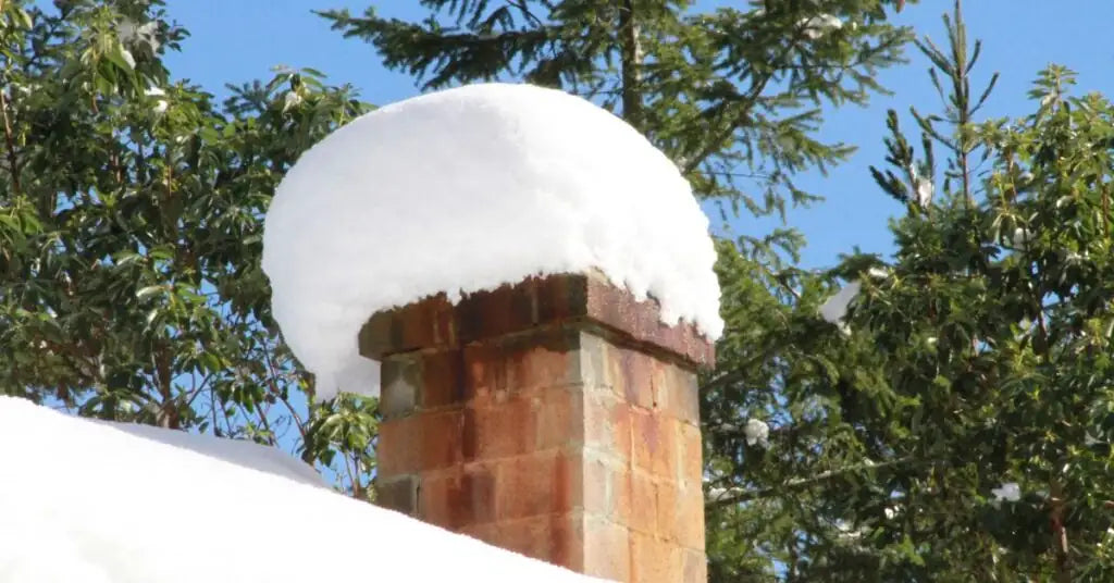 Snow-covered uncapped chimney crown showing water infiltration risk in winter