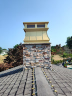 Custom gold anodized aluminum chimney cap installed on stone masonry chimney, rooftop view — curved panel design with stainless spark screen, handcrafted by Archaic Metal