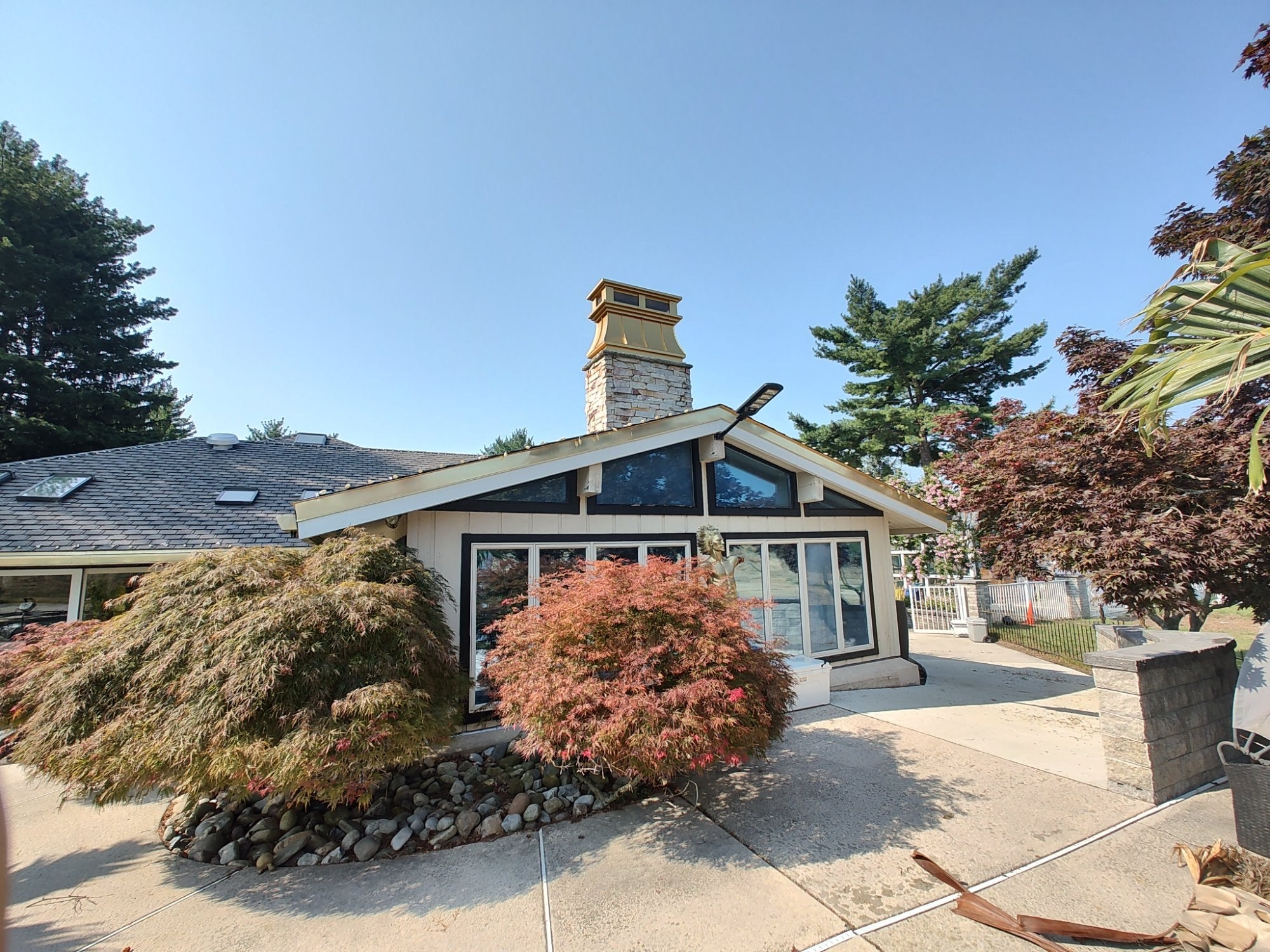 Gold anodized aluminum chimney cap installed on mid-century modern home — full house view showing curved panel chimney topper on stone chimney, by Archaic Metal