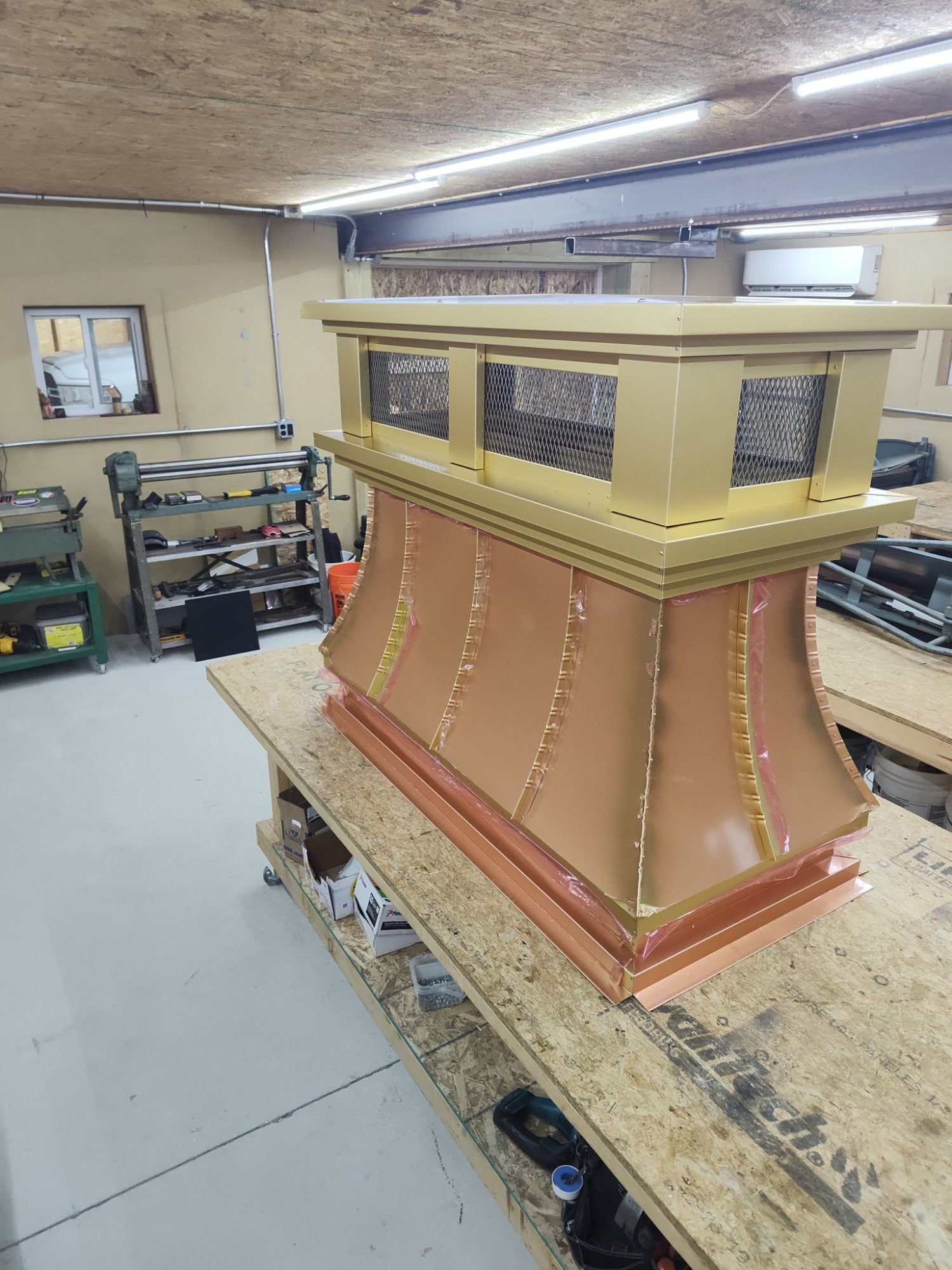 Three-quarter view of curved panel anodized aluminum chimney cap on workbench — crown molding detail and curved side panels visible, handcrafted by Archaic Metal