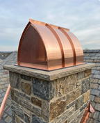 Arched Gothic Copper Chimney Flue Cover on a stone chimney with a blue sky and slate roof. 