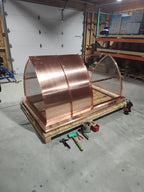 Large custom curved panel chimney cap in 16oz copper on a shipping crate — concave mansard profile with stainless steel spark screen, fabricated in the Archaic Metal shop in Berlin, NJ