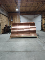 Large custom multi-flue curved panel chimney cap in 16oz copper on a shipping crate — front view showing concave mansard roof panels, fabricated in the Archaic Metal shop in Berlin, NJ