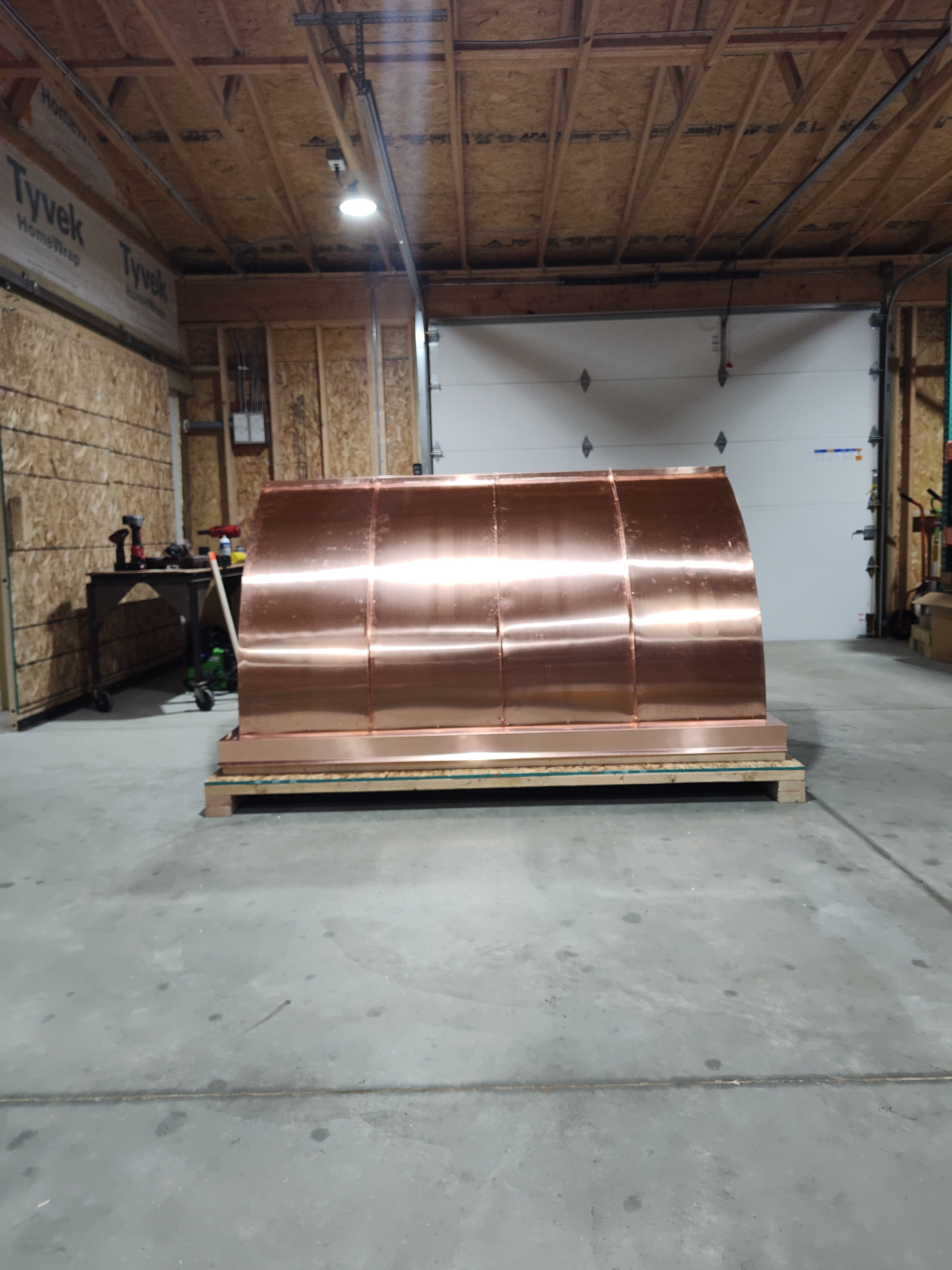 Large custom multi-flue curved panel chimney cap in 16oz copper on a shipping crate — front view showing concave mansard roof panels, fabricated in the Archaic Metal shop in Berlin, NJ