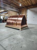 Large custom multi-flue curved panel chimney cap in 16oz copper on a shipping crate — front view showing concave mansard roof panels, fabricated in the Archaic Metal shop in Berlin, NJ