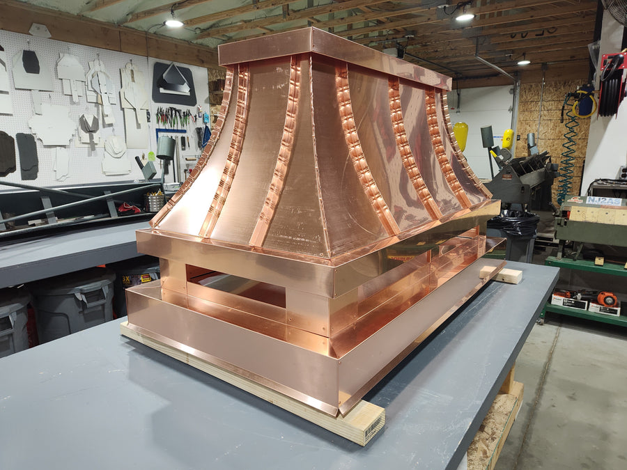 Large custom copper chimney shroud with multi-panel curved design on workbench, hand-fabricated by Archaic Metal