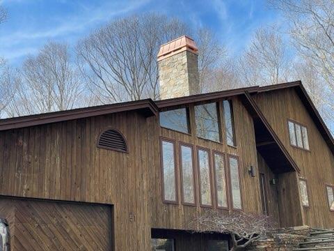 A-frame wood home with custom copper chimney cap on stone masonry chimney — hand-fabricated by Archaic Metal

