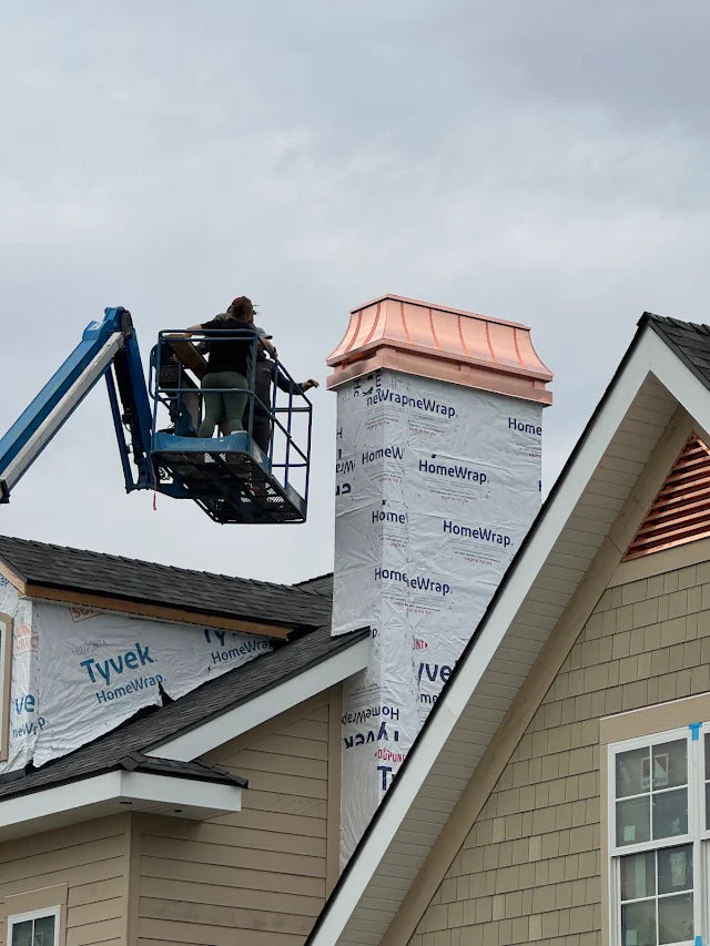 Custom copper chimney cap being installed via bucket truck on new construction home during build — Archaic Metal fabricated