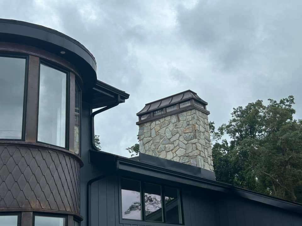 Custom copper chimney cap with bronze patina on stone chimney above modern copper-clad curved roofline — hand-fabricated by Archaic Metal
