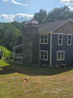 Custom copper chimney cap on tall stone chimney of blue shingle-sided home — hand-fabricated by Archaic Metal