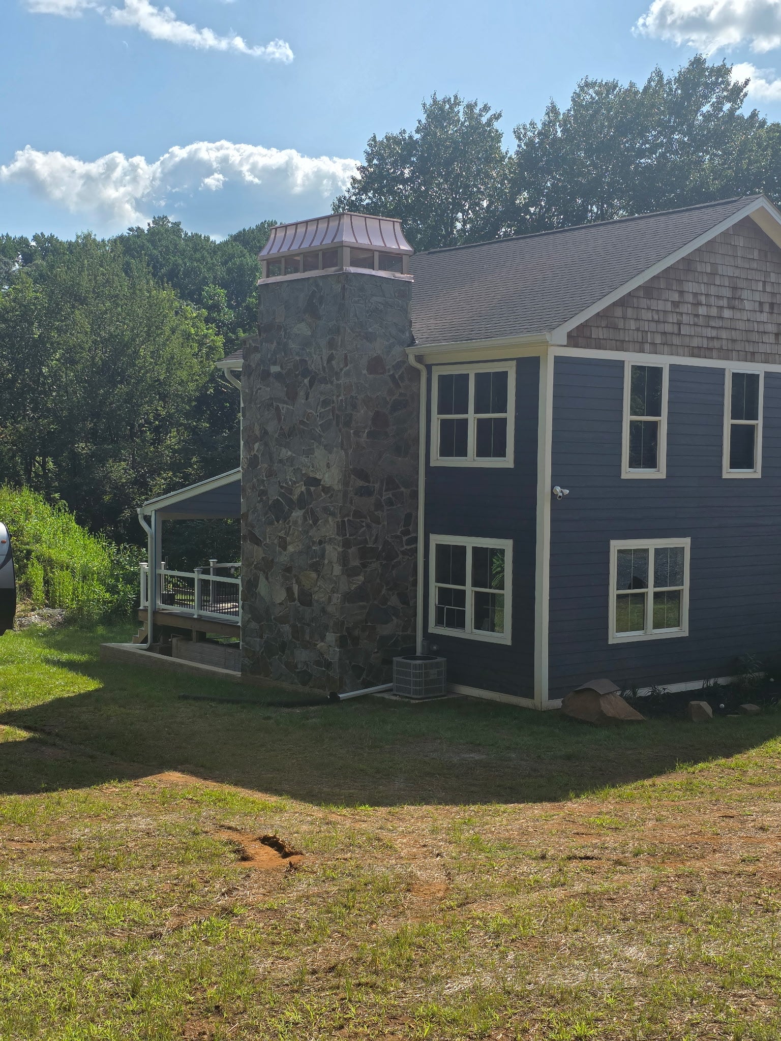 Custom copper chimney cap on tall stone chimney of blue shingle-sided home — hand-fabricated by Archaic Metal