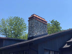 Custom copper straight panel chimney cap on tall stone masonry chimney with slate roof — hand-fabricated by Archaic Metal