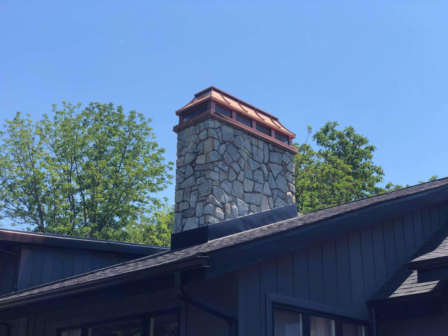 Custom copper straight panel chimney cap on tall stone masonry chimney with slate roof — hand-fabricated by Archaic Metal