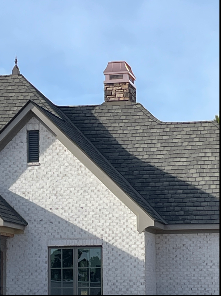 Custom copper chimney cap on stone chimney above white brick home with slate roof — hand-fabricated by Archaic Metal