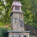 Custom copper chimney cap on stone outdoor fireplace column with decorative sculpture — hand-fabricated by Archaic Metal
