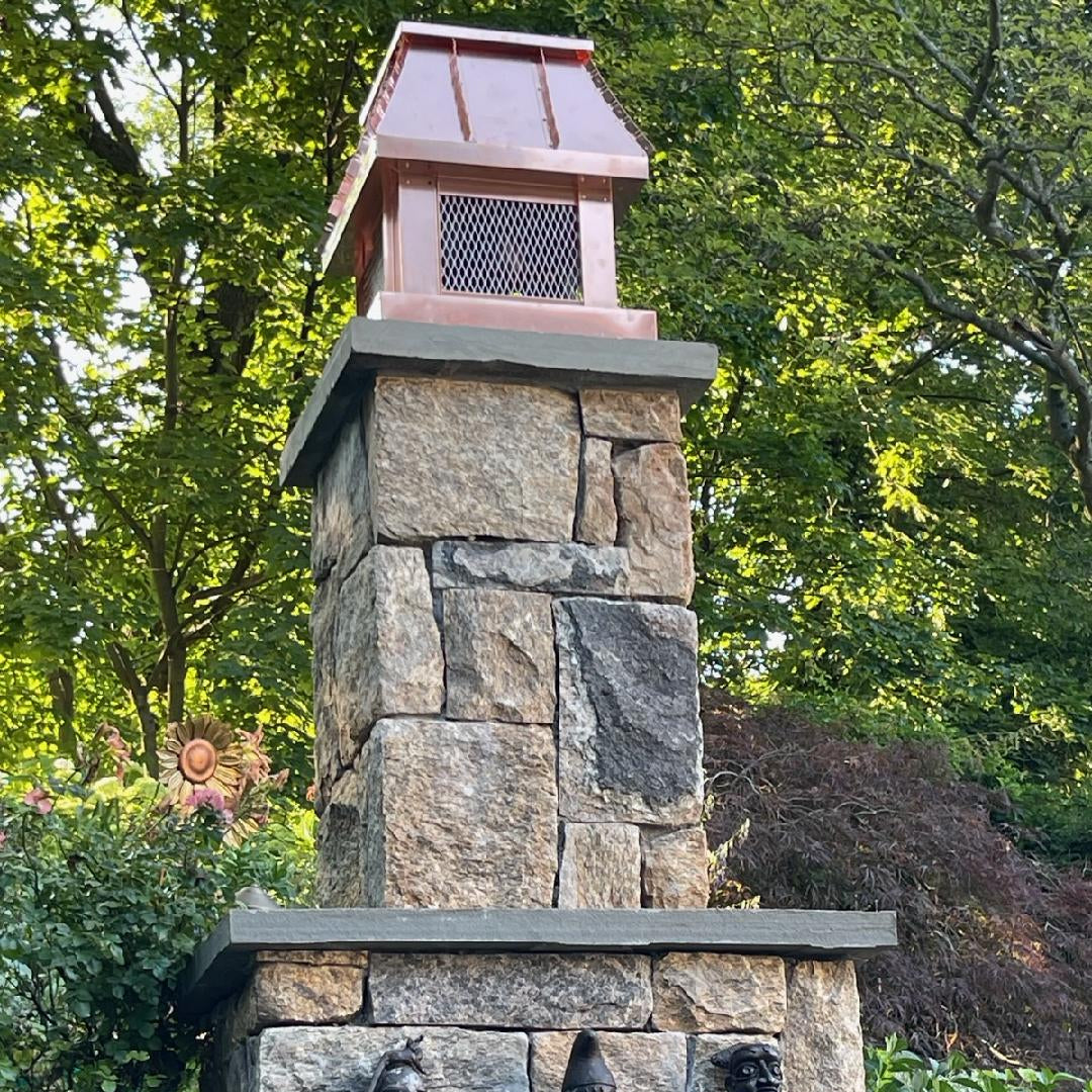 Custom copper chimney cap on stone outdoor fireplace column with decorative sculpture — hand-fabricated by Archaic Metal