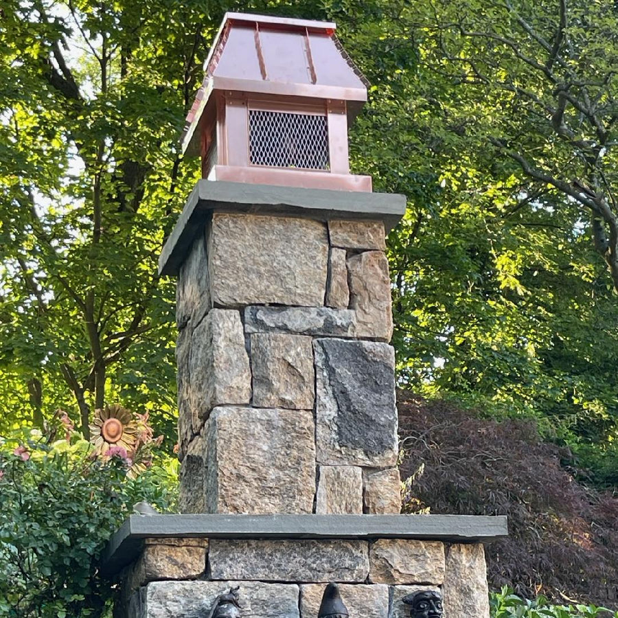 Custom copper chimney cap on stone outdoor fireplace column with decorative sculpture — hand-fabricated by Archaic Metal