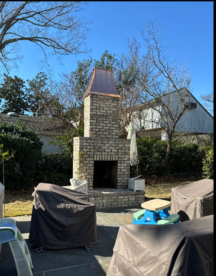 Custom copper chimney cap on stone outdoor fireplace in residential backyard patio setting — hand-fabricated by Archaic Metal