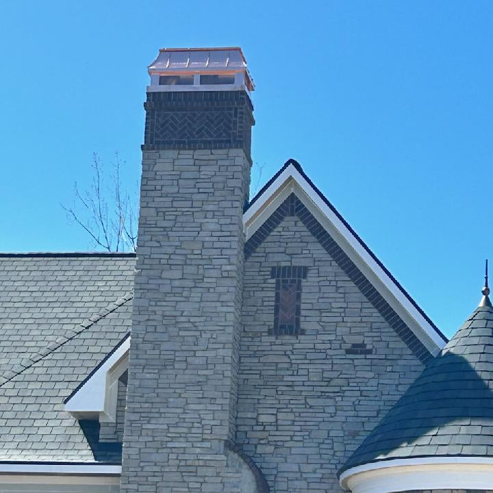 Custom copper chimney cap on tall stone chimney of luxury new construction home — hand-fabricated by Archaic Metal