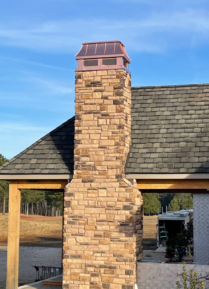 Custom copper chimney cap on tall narrow stone chimney above timber frame outdoor pavilion — hand-fabricated by Archaic Metal