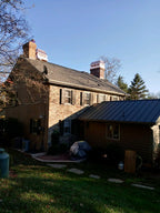 Historic stone home with standing seam metal roof and multiple copper chimney caps installed — hand-fabricated by Archaic Metal