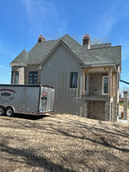 New construction stone and board-batten home with copper chimney caps installed — Archaic Metal delivery trailer on site