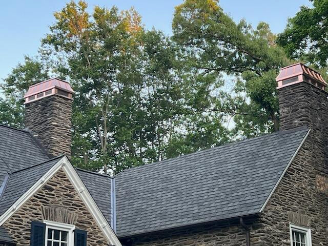 Matching pair of custom copper chimney caps on twin stone masonry chimneys — hand-fabricated by Archaic Metal