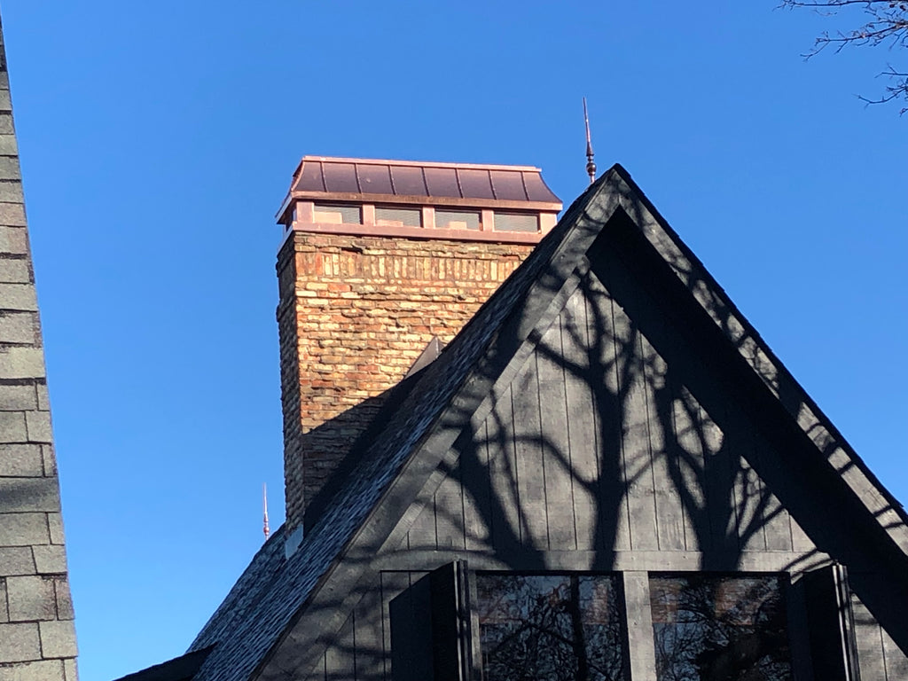 Custom copper chimney shroud with spark screen on brick chimney above dramatic steep gable roofline — hand-fabricated by Archaic Metal