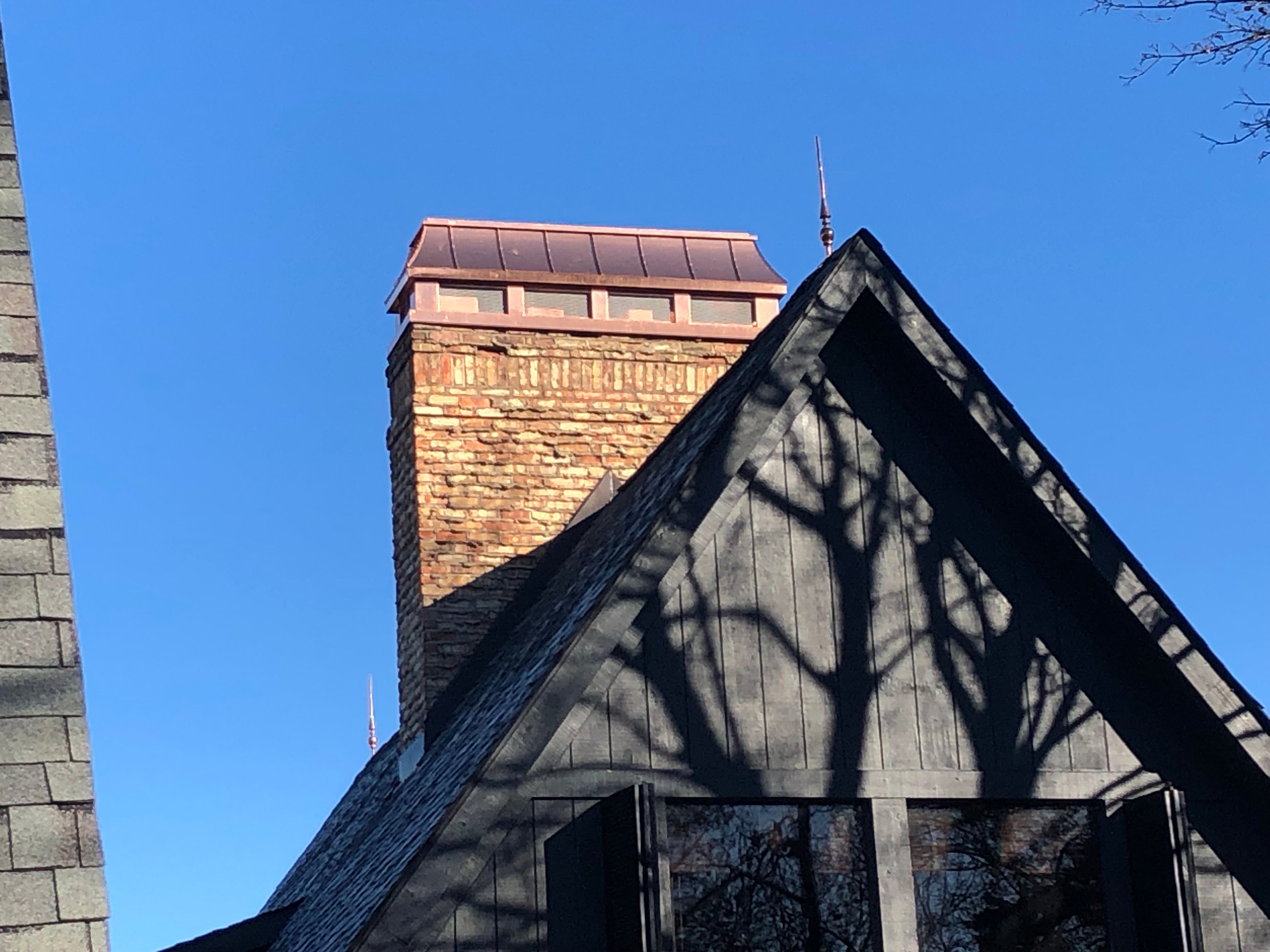 Custom copper chimney shroud with spark screen on brick chimney above dramatic steep gable roofline — hand-fabricated by Archaic Metal