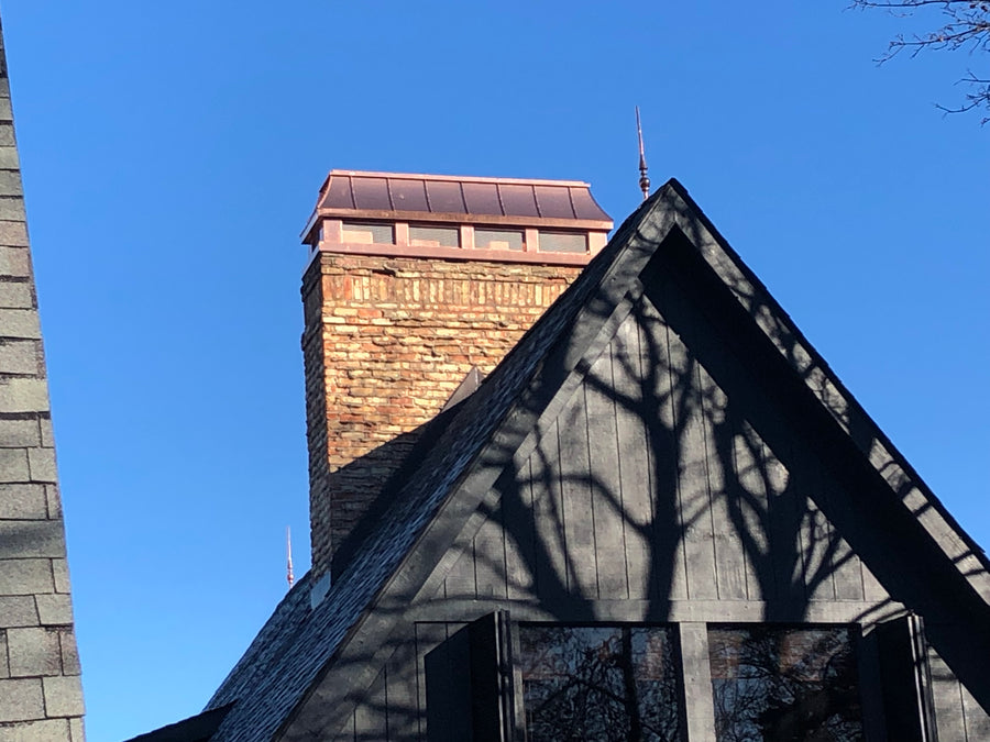 Custom copper chimney shroud with spark screen on brick chimney above dramatic steep gable roofline — hand-fabricated by Archaic Metal
