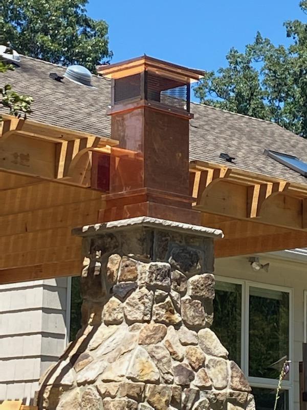 square copper chimney pot on a outdoor fireplace made of fieldstone with a nice wooden pergola