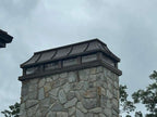 Custom copper curved panel chimney cap with natural bronze patina on stone masonry chimney — first cap fabricated at Archaic Metal Berlin NJ shop