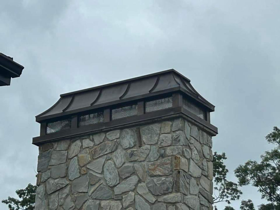 Custom copper curved panel chimney cap with natural bronze patina on stone masonry chimney — first cap fabricated at Archaic Metal Berlin NJ shop