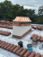 Custom copper curved panel chimney cap on stucco chase during clay tile roof installation — hand-fabricated by Archaic Metal