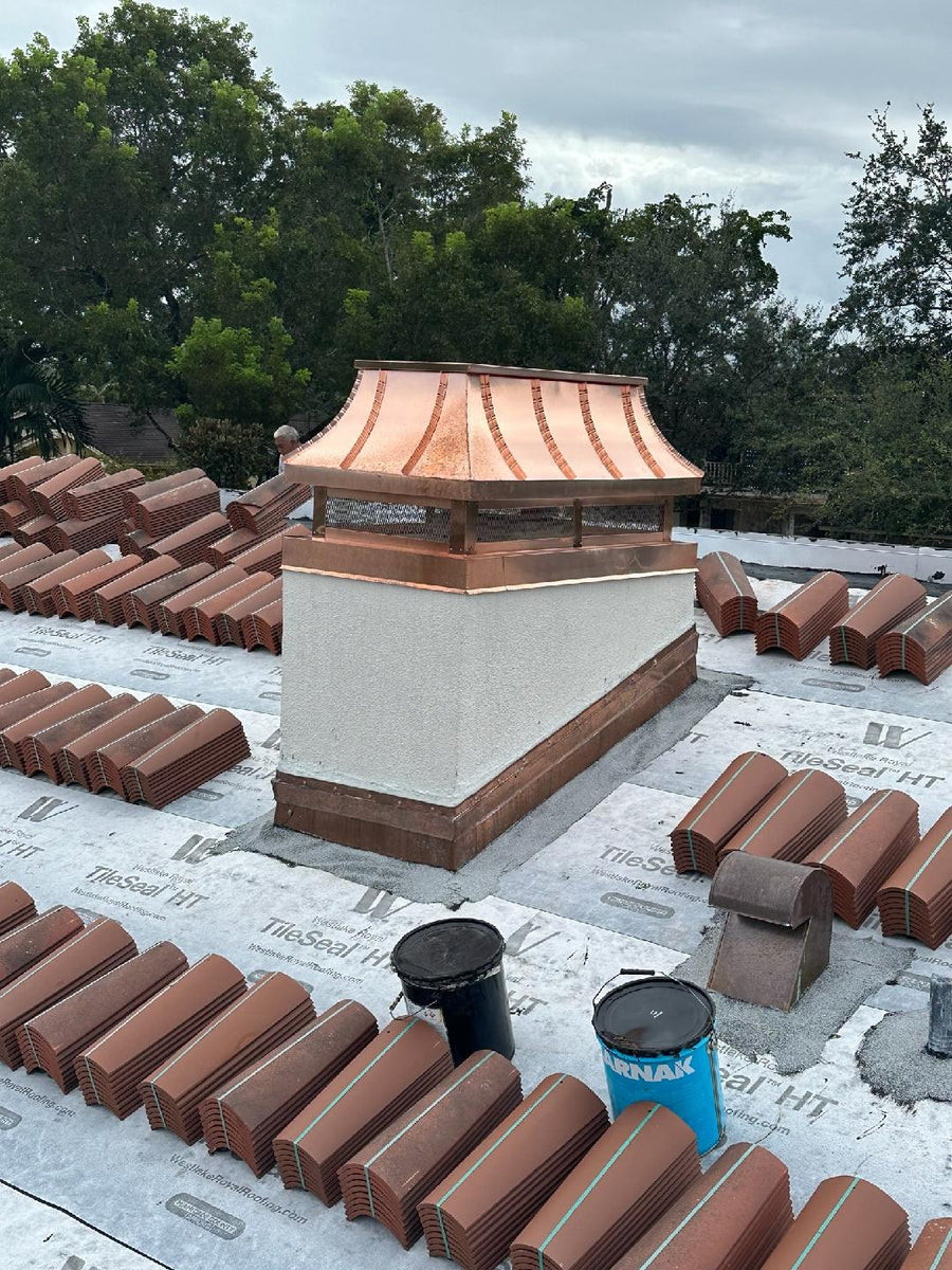 Custom copper curved panel chimney cap on stucco chase during clay tile roof installation — hand-fabricated by Archaic Metal