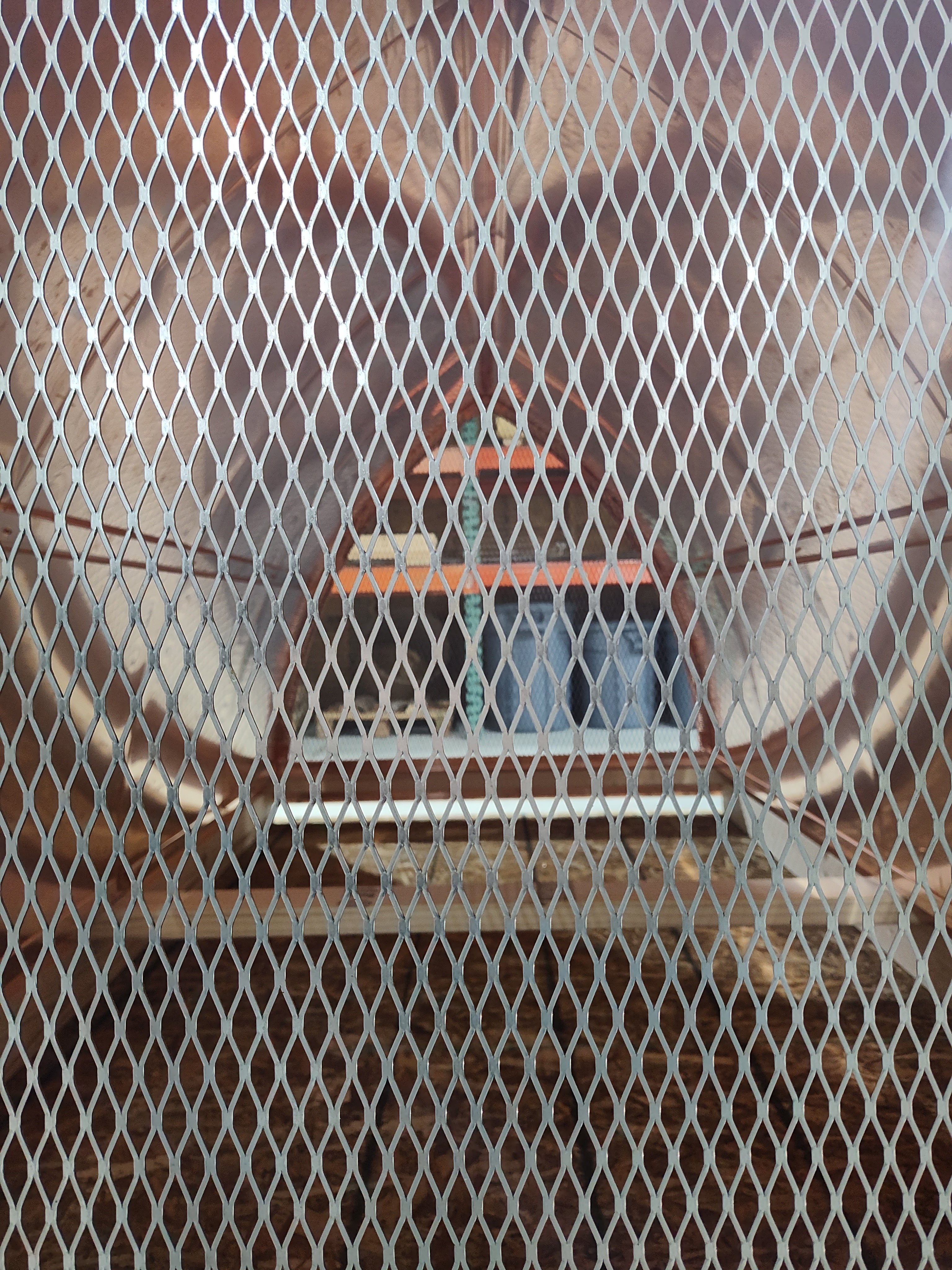 Interior detail view looking through the 18-gauge expanded stainless steel spark screen of a curved panel chimney cap — close-up showing screen mesh quality and cap base structure, fabricated by Archaic Metal in Berlin, NJ