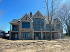 Large two-story stone luxury home under construction with uncapped chimneys — custom chimney caps fabricated to order by Archaic Metal