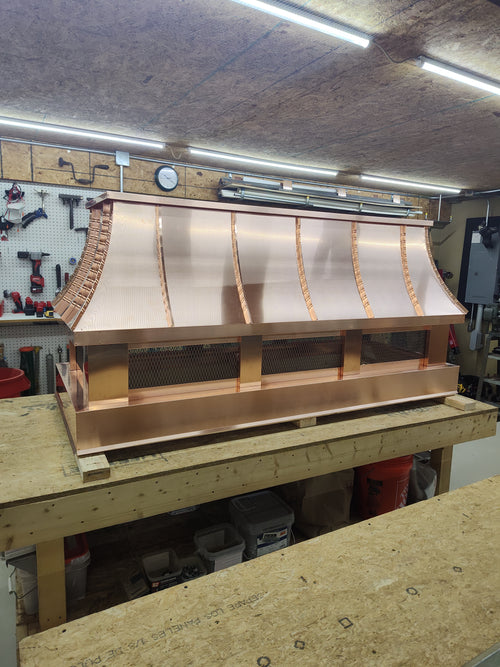 Arched top custom copper chimney cap with stainless steel spark screen on workbench

