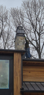 Contractor installing custom Kynar black chimney cap on stone chimney of modern wood and steel home — hand-fabricated by Archaic Metal