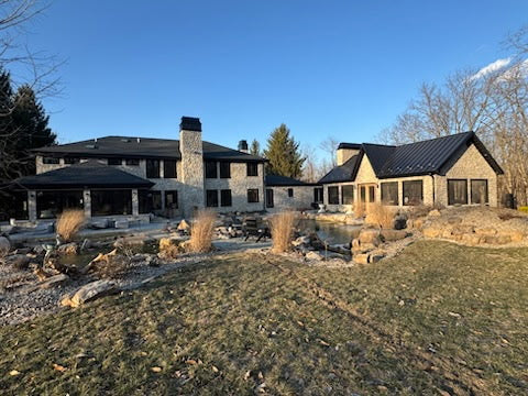 Custom Kynar black chimney cap on stone chimney of luxury home with standing seam roof and waterfront setting — hand-fabricated by Archaic Metal