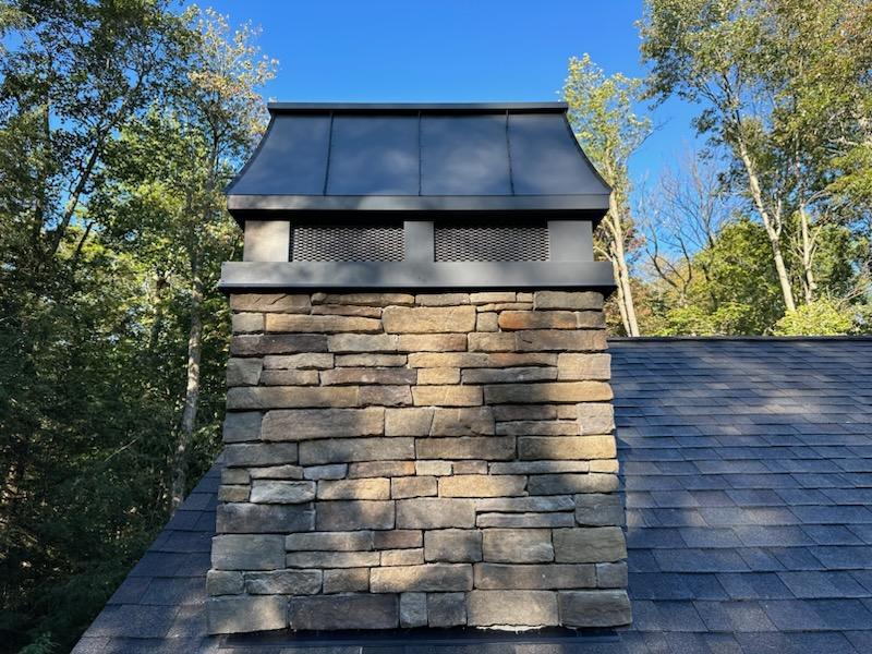 Custom Kynar black aluminum chimney shroud with spark screen on stone masonry chimney — hand-fabricated by Archaic Metal