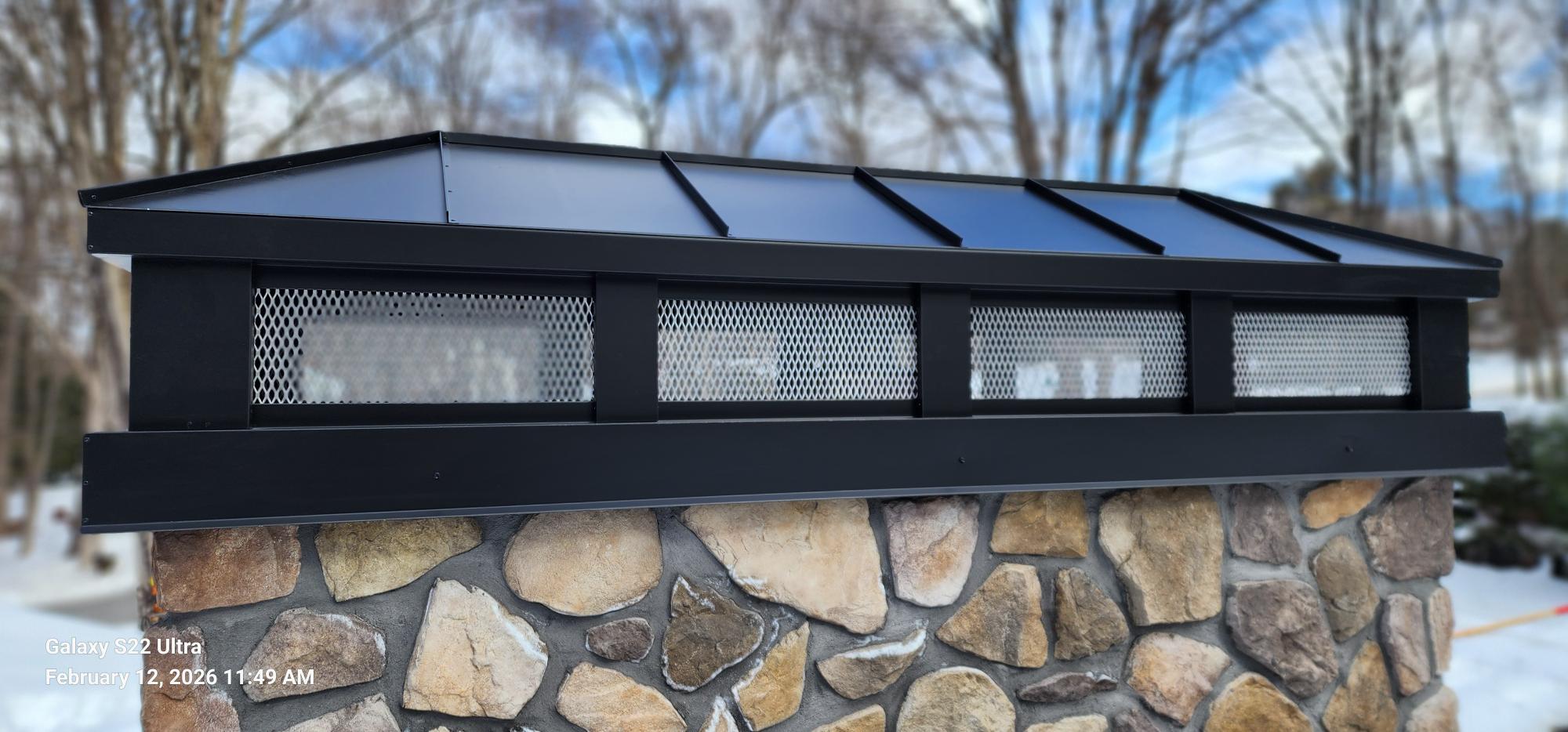 Custom Kynar black hip and ridge chimney cap with stainless steel spark screen on stone masonry chimney — hand-fabricated by Archaic Metal