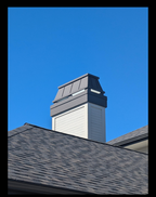 Custom Kynar black straight panel chimney cap on wood-framed chase above shingle roof — hand-fabricated by Archaic Metal