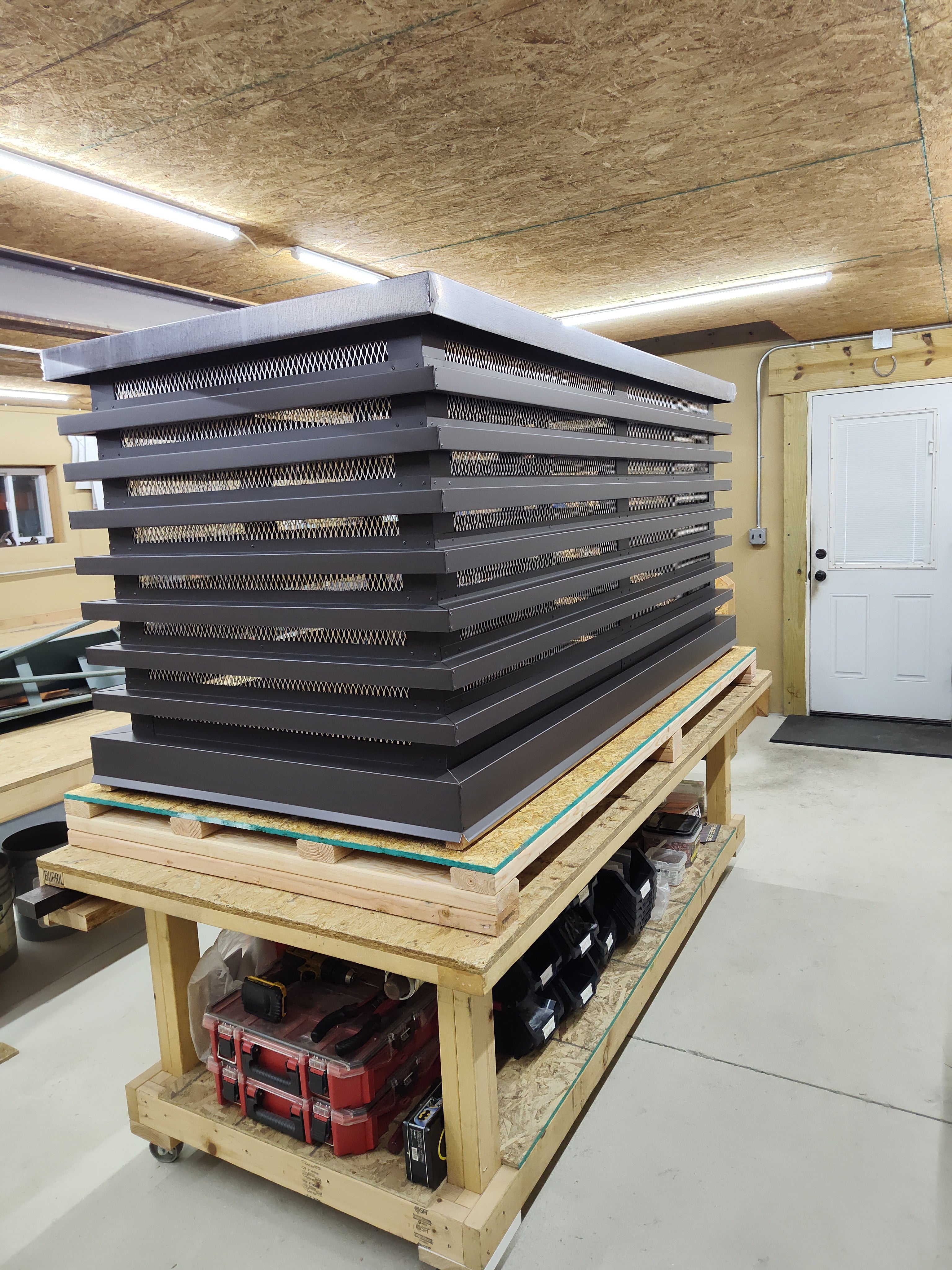 Custom louvered chimney caps with stainless steel spark screens stacked in Archaic Metal shop