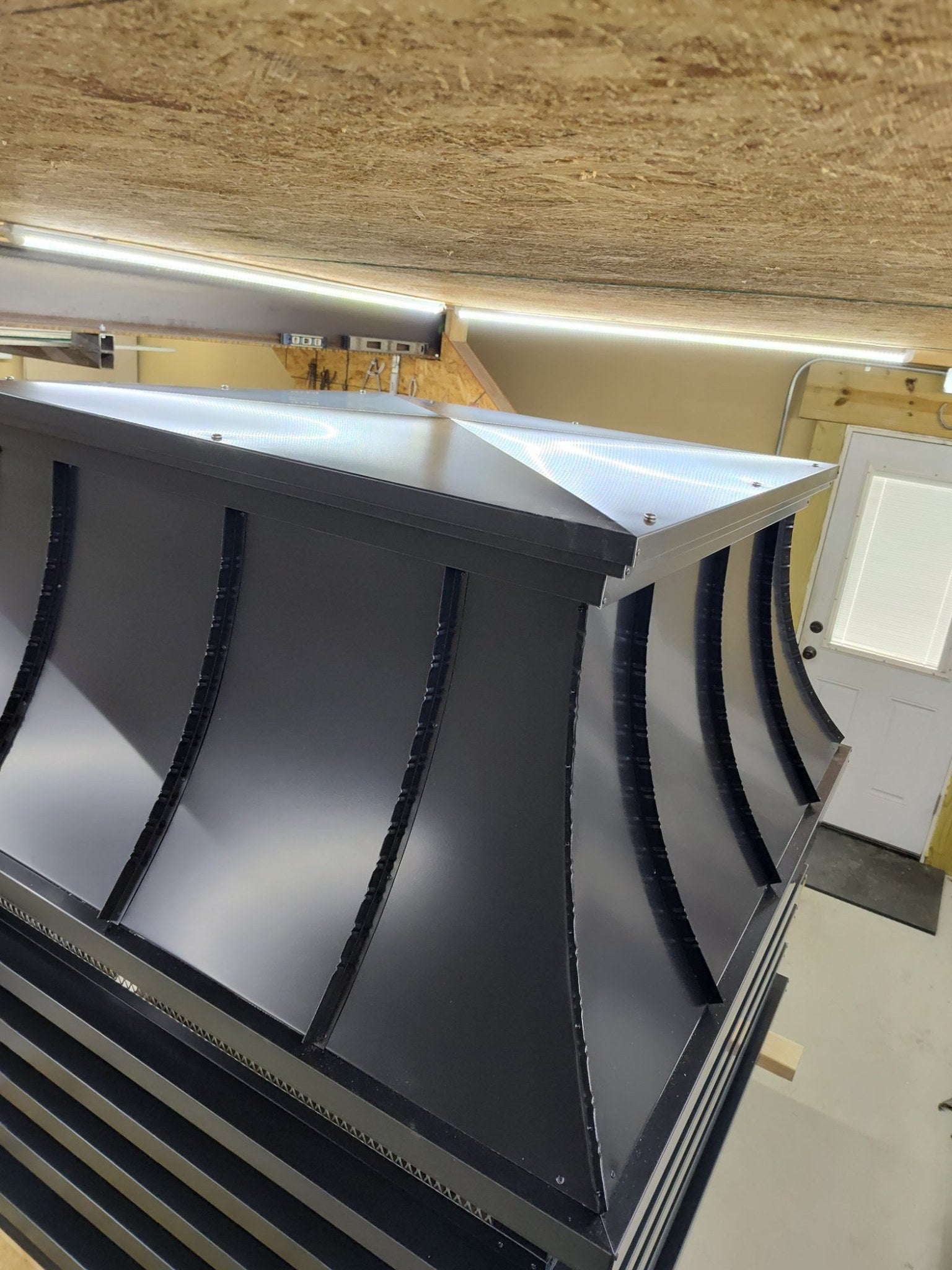 Close-up detail of curved panel section and solid removable lid on a custom modern louvered chimney cap — Kynar aluminum fabrication by Archaic Metal
