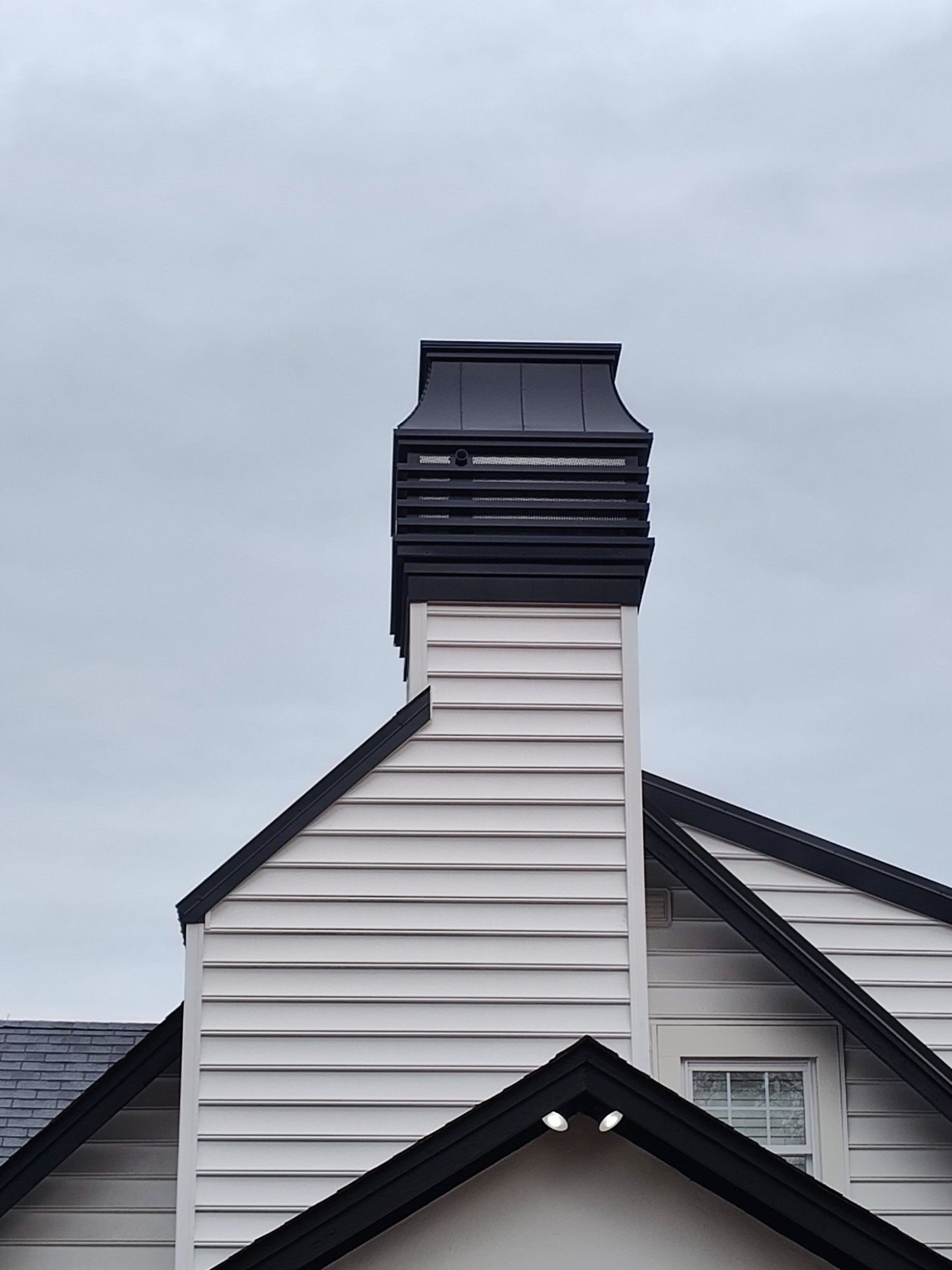 Modern louvered chimney cap installed on wood-framed prefab chimney chase — black Kynar aluminum custom cap by Archaic Metal