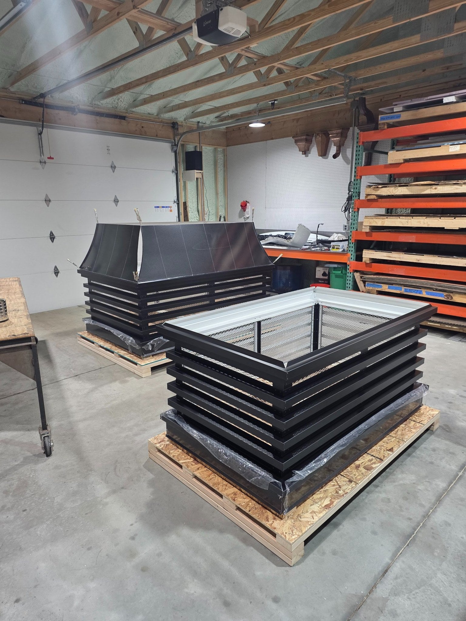 Two custom modern louvered chimney caps in fabrication shop — one with removable lid removed showing open-top construction, Archaic Metal Berlin NJ